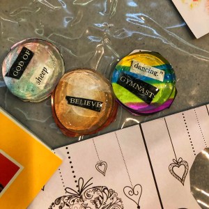 Glass beads with magazine cutout background. Beads say "God of Sheep", "Believe" and "Dancing Gymnast"
