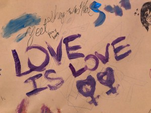 Love is Love with two venus symbols painted on brown paper.