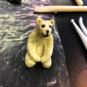 Clay polar bear sits on hind legs with front paws clasped.
