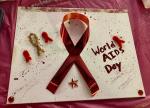 Large red ribbon, smaller pipe cleaner ribbons and glitter on a World AIDS Day poster.